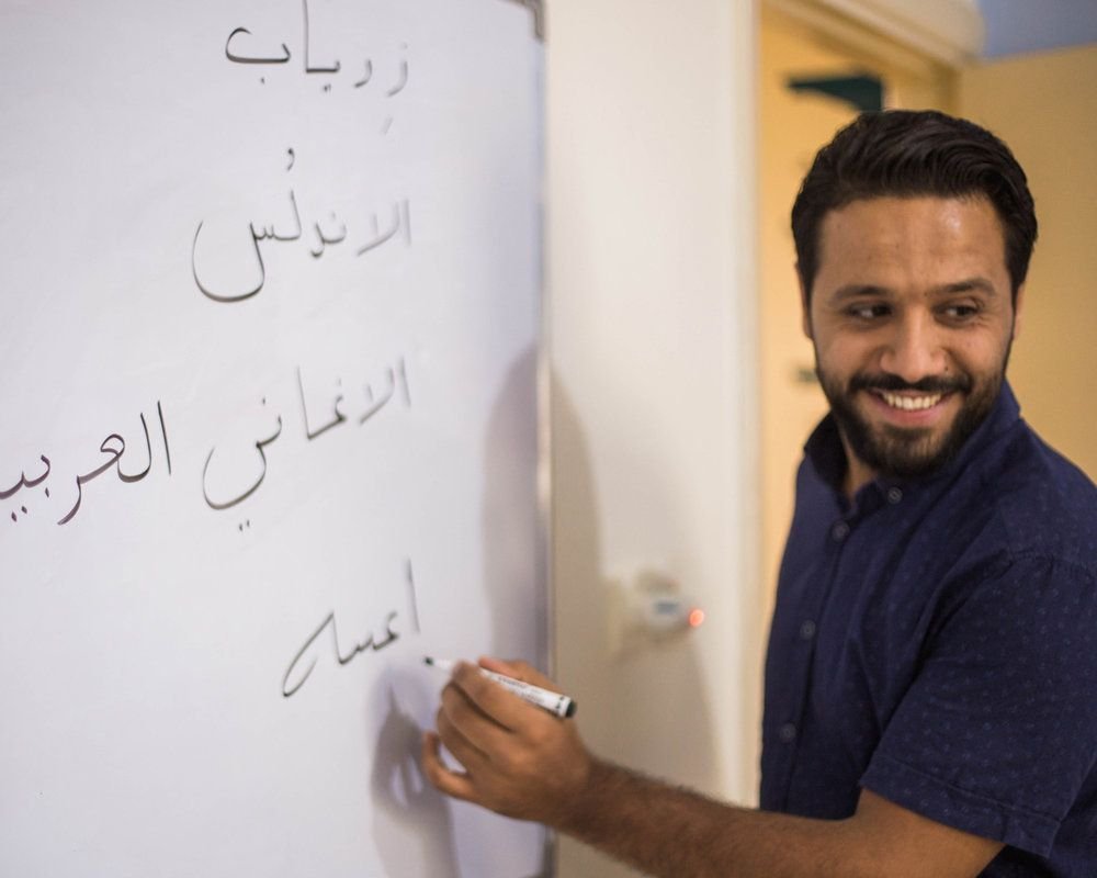 Arabic teacher smiling while writing Arabic words on a whiteboard